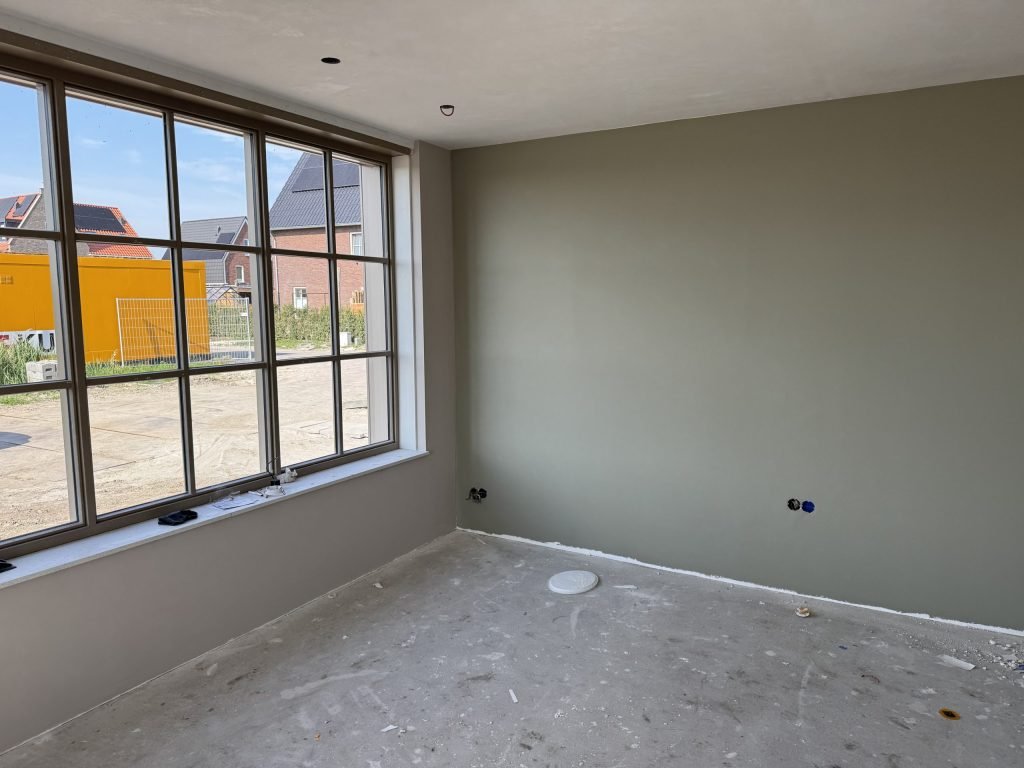 Wand in een grijsgroene tint naast een groot roedenraam in een nieuw huis