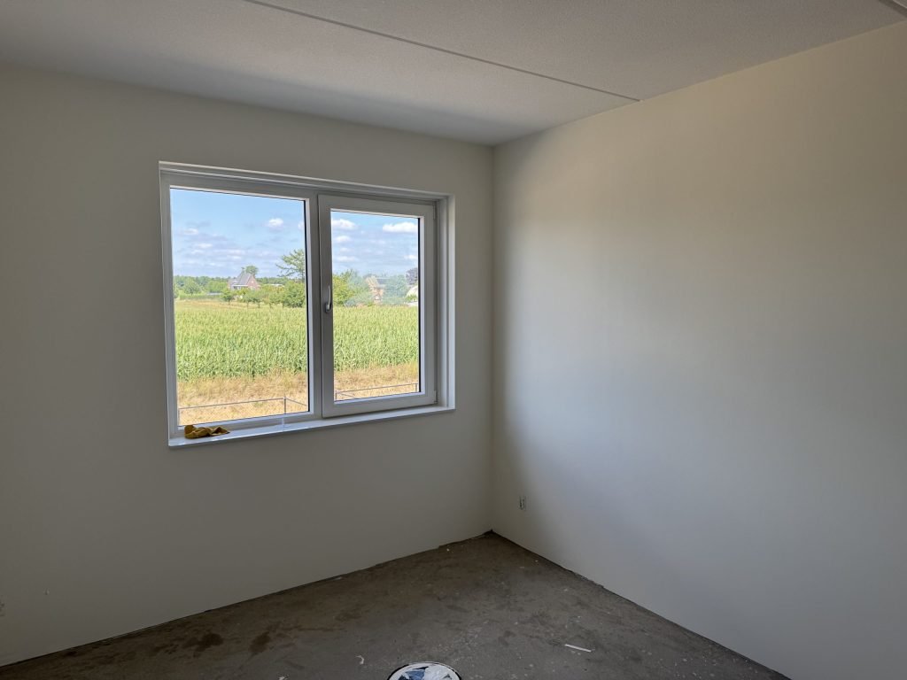 Lege slaapkamer met strakke lichte wanden en uitzicht over een maisveld