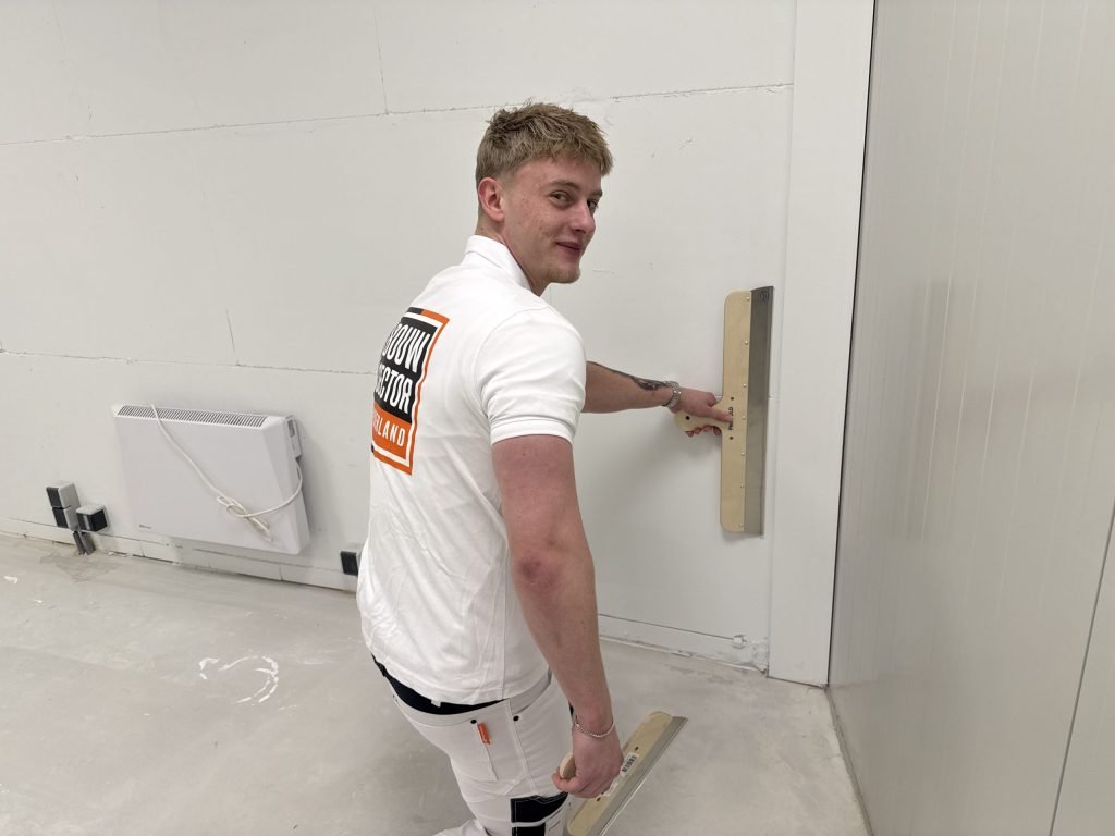 Vakman van Bouwsector Nederland trekt een wand glad met een brede spaan voordat het behang erop gaat